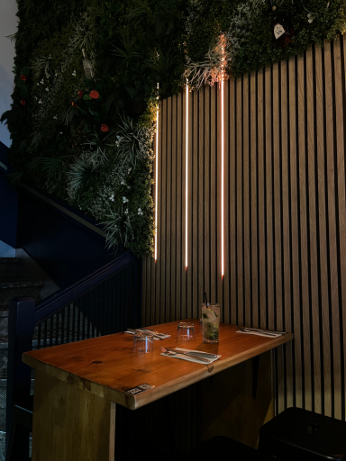 Table en bois avec un verre, décorée de plantes et d'éclairage suspendu.